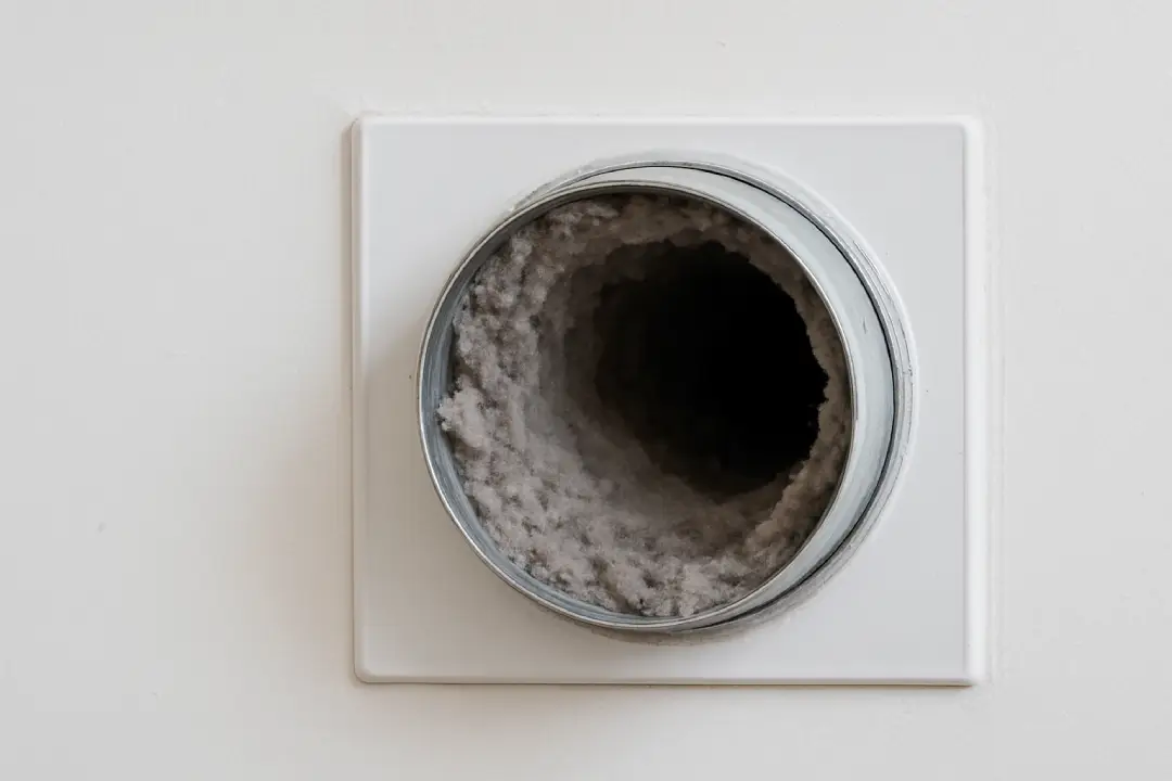 Close-up of a residential dryer vent clogged with lint inside a white wall panel